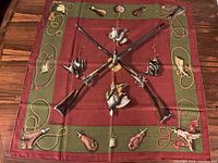 Full view of the square scarf laid flat showing overall red field, olive border and hunting motif.