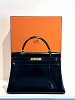 Front view of black Hermès Kelly 32 Retourne handbag against orange Hermès box