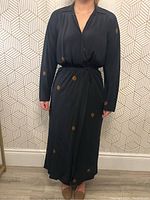 Front view of the black wrap dress on model against geometric wallpaper