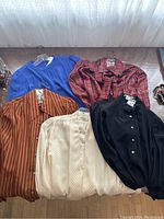 Group shot of five Saint Laurent silk blouses laid flat on a table showing all colors and patterns