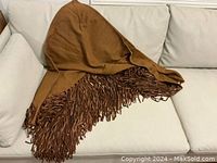 Shawl draped on couch showing triangular shape and fringe.