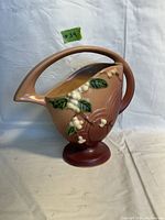 Front view of antique Roseville basket vase showing handle, floral relief, and pedestal base.