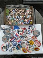 Overview of large collection of vintage political pinback buttons spread on a white board and inside a box; includes multiple candidate buttons from mid-20th century U.S. politics.