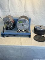 Side view of the LORTONE rotary tumbler base showing motor and rotating drum barrel, with two drum barrel assemblies on the right including lids and liners.
