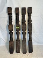 Lot of four antique wooden balusters laid flat on white background showing full length and carved details.