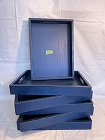 Stacked view of the seven blue wooden trays showing thickness and edges with side handles.