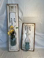 Pair of vintage style wall-mounted vases with distressed white baluster designs on wood plaques, each holding blue mason jars, one with flowers