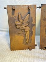 Front side of one mold plate with detailed raised relief of Tinker-Bell in profile with wings, dress, and upraised arm.
