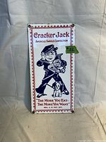 Full view of vintage porcelain Cracker Jack sign with mascot and text, showing overall condition including rust spots on corners.