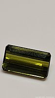 Close-up photo of single rectangular emerald-cut natural green tourmaline gemstone with bright green color and visible internal characteristics.