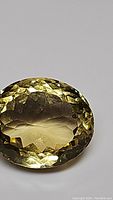 Close-up image of an oval-shaped, faceted natural citrine gemstone with yellow hues and pristine clarity showing checkered facet pattern on top.