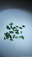 Photo showing a collection of small marquis cut deep green African emerald gemstones illuminated to show color and some inclusions.