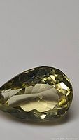 Close-up image of a single pear shaped lemon yellow citrine gemstone with multiple facets showing high clarity.