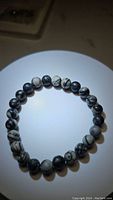 Close-up photo of the natural black web jasper bead bracelet, showing round beads with black and white web-like patterns, laid in a circular formation.