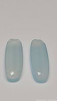 Pair of natural blue chalcedony gemstones with fancy pill cut and icy blue color, smooth surface, displayed side by side.