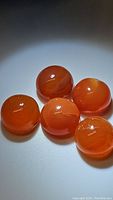 Five round polished mandarin orange Carnelian cabochon gemstones laid on a flat surface showing smooth glossy finish and natural inclusions.
