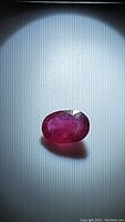Close-up photo of deep pink oval sapphire with natural inclusions, showing color and oval cut shape on white background.