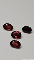 Four natural garnet gemstones on white background, oval cut with red hues visible.