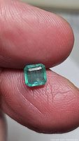 Close-up image of the emerald cut emerald held between fingers, showing color and clarity details.