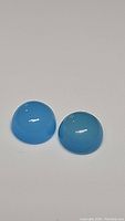Two round cabochon icey blue chalcedony stones on white background, showing translucent color and smooth polished surface.