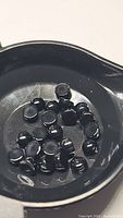 Photo showing multiple small round jet black onyx cabochon gemstones placed in a black plastic dish, highlighting the smooth polished surface and uniform size.