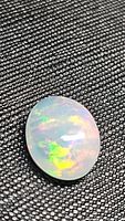 Oval opal cabochon on textured black background showing green and yellow flash