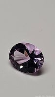 Clear close-up photo of the oval cut bright purple amethyst gemstone showing faceting and clarity.