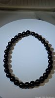 Photo of a natural black onyx stretchy bead bracelet laid flat in a circular shape on a white surface, showing the smooth, polished round beads with a glossy black finish.