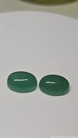 Two natural green onyx oval cabochons photographed on white background showing smooth polished surface and translucent green color.