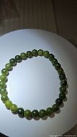 Top view of the circular natural green jade bead bracelet on white background showing the color variation of beads.