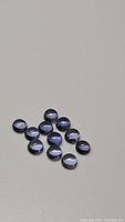 Twelve small round purple iolite cabochon gemstones arranged on a flat surface, showing smooth polished domed tops and color details.