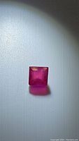 Front view of the square cut deep pink red ruby gemstone under lighting, showing clarity and cut detail.