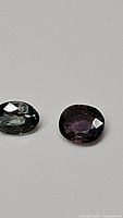 Close-up image showing the green and purple oval cut sapphires side by side on a gray background, illustrating shape, cut, and color.