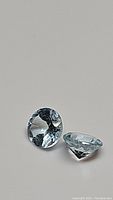 Close-up photo of two round diamond cut sky blue topaz gemstones showing clarity and cut.