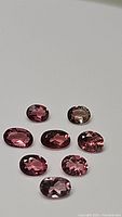 Eight oval pink tourmaline gemstones arranged in a cluster on a plain background showing size, color and cut.