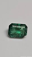Photograph of a 0.67 carat natural Zambian emerald gemstone, emerald cut with visible internal inclusions, resting on a neutral background.