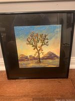 Framed painting of a Joshua tree with desert mountains and sky in colorful tones, photographed front view.