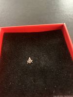 Single gold-tone Masonic lapel pin displayed on black background inside red box.