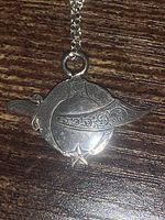 Close-up photo of the sterling silver Masonic pendant showing detailed engravings of a helmet and star design with decorative filigree.