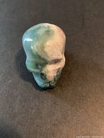 Close-up front view of small carved stone skull showing green and cream polished surface