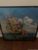 Framed original painting showing a butterfly-wing sailboat on water, with animal-shaped clouds and silhouetted figures on shore.
