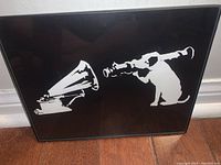 Framed black and white street art print showing a dog blowing a trumpet facing a gramophone horn.