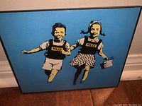 Framed street art print showing stencil image of two children holding hands, wearing police vests, with blue background.