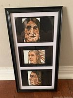 Photo of all three original Indigenous paintings displayed vertically in a single black frame with white matting against a wall
