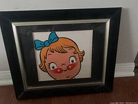Front view of framed vintage Campbell Soup girl advertising art showing the cartoon girl's head with blue bow and rosy cheeks.