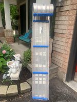 Full view of vintage aluminum toboggan shown upright against a brick wall and garden background, emphasizing its length, supports, and overall condition.