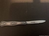 Image of full cutting utensil showing ornate silver floral handle and slim blade.