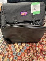 Front view of the black Thumper Versa Pro bag showing flap closed with two buckle straps and thick ribbed black protective panel on front pocket.