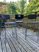Set of three black metal frame bar stools with molded plastic seats and backrests, situated on wooden deck