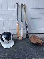 Front view of 3 baseball bats, white helmet with number 24, brown Easton glove, all items placed upright or flat on ground.